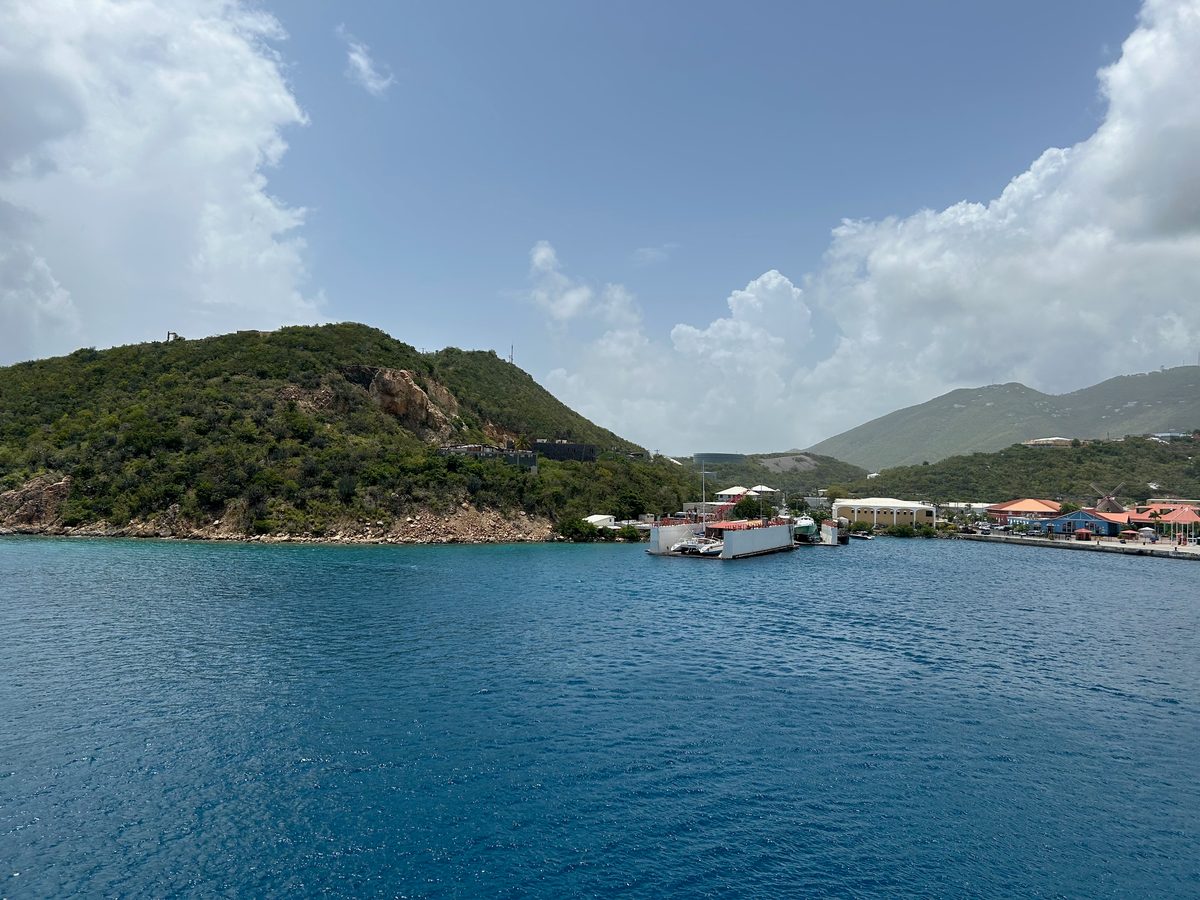 A green hillside and a small harbor town across deep blue Caribbean water