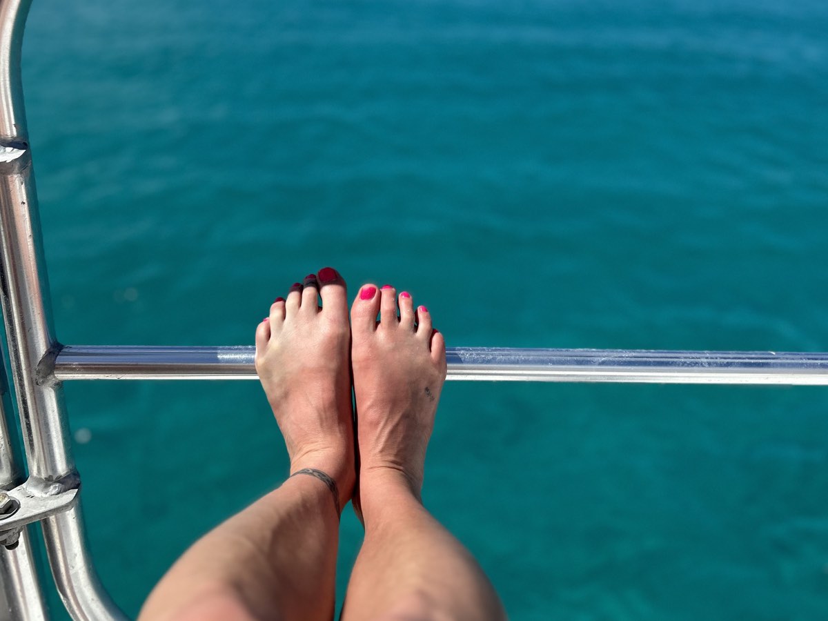 Feet up on a ship’s rail above turquoise water
